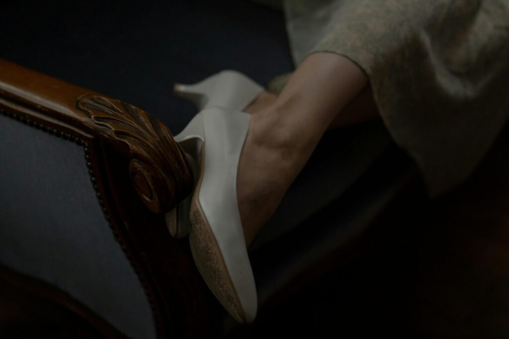 Close-up of stylish white high heels on a vintage wooden chair armrest.